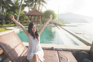 Closeup portrait of pretty girl raise her hands enjoying sunlight on tropical beach, luxury spa resort, travel and tourism concept - Bali Dive Resort