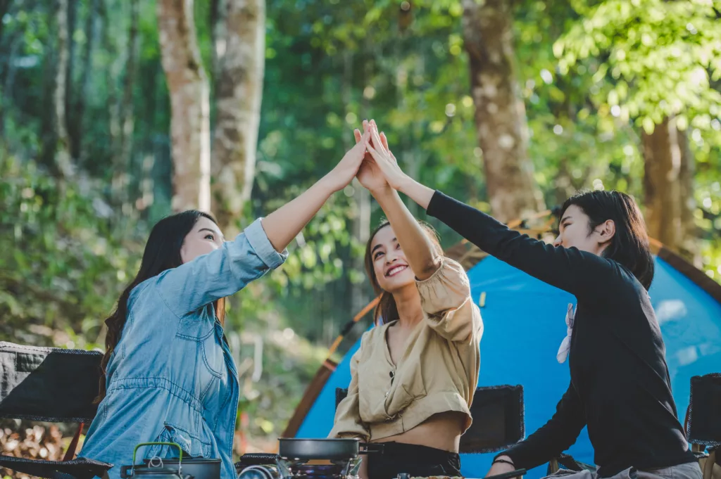 Group of women giving five to each other on camping with toothy smile and happy together at front of camping tent in forest - Bali Diving Resort