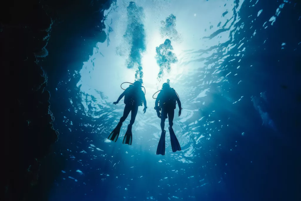 Underwater view of a scuba diver exploring a cave. The diver is wearing a wetsuit and fins, and is surrounded by colorful fish and coral - Bali Dive Resort