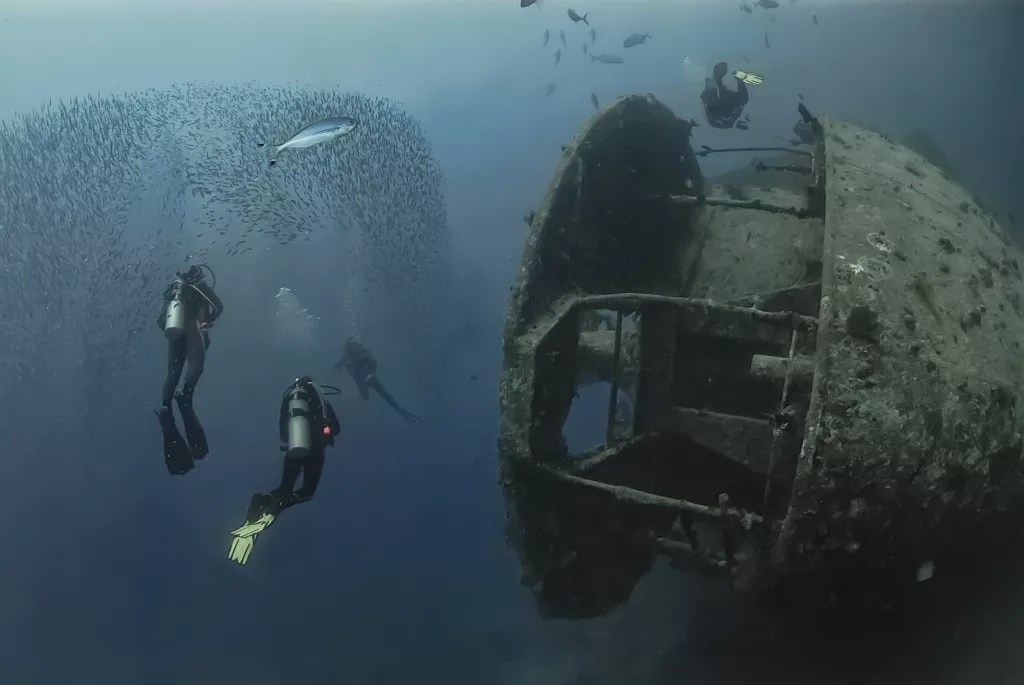 Divers swim alongside the legendary SS Thistlegorm, a World War II shipwreck in the Red Sea, teeming with marine life and historical intrigue - Boga Wreck