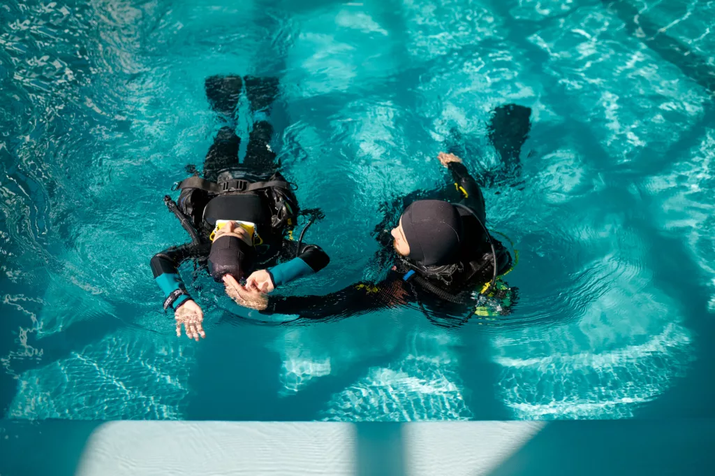 Female diver and male instructor in scuba gear, lesson in diving school. Teaching people to swim underwater, indoor swimming pool interior on background - Bali Dive Resort