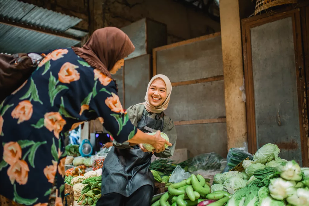 happy asian green grocery seller helping her customer choosing vegetable