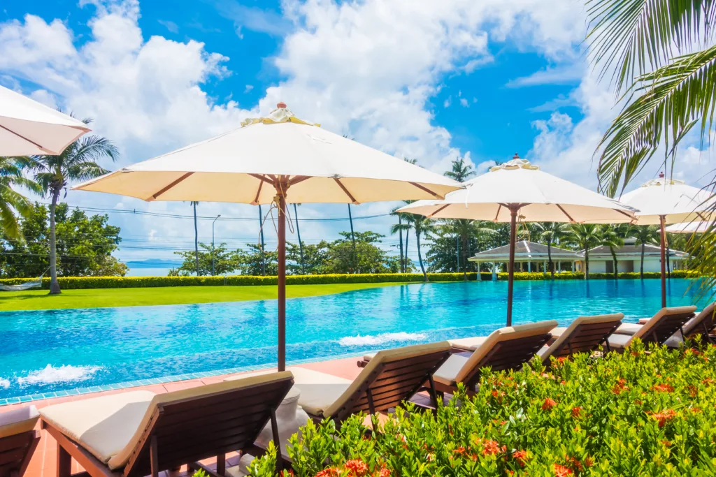 Beautiful luxury umbrella and chair around outdoor swimming pool in hotel and resort with coconut palm tree on blue sky - Boost up color Processing - Bali Dive Resort